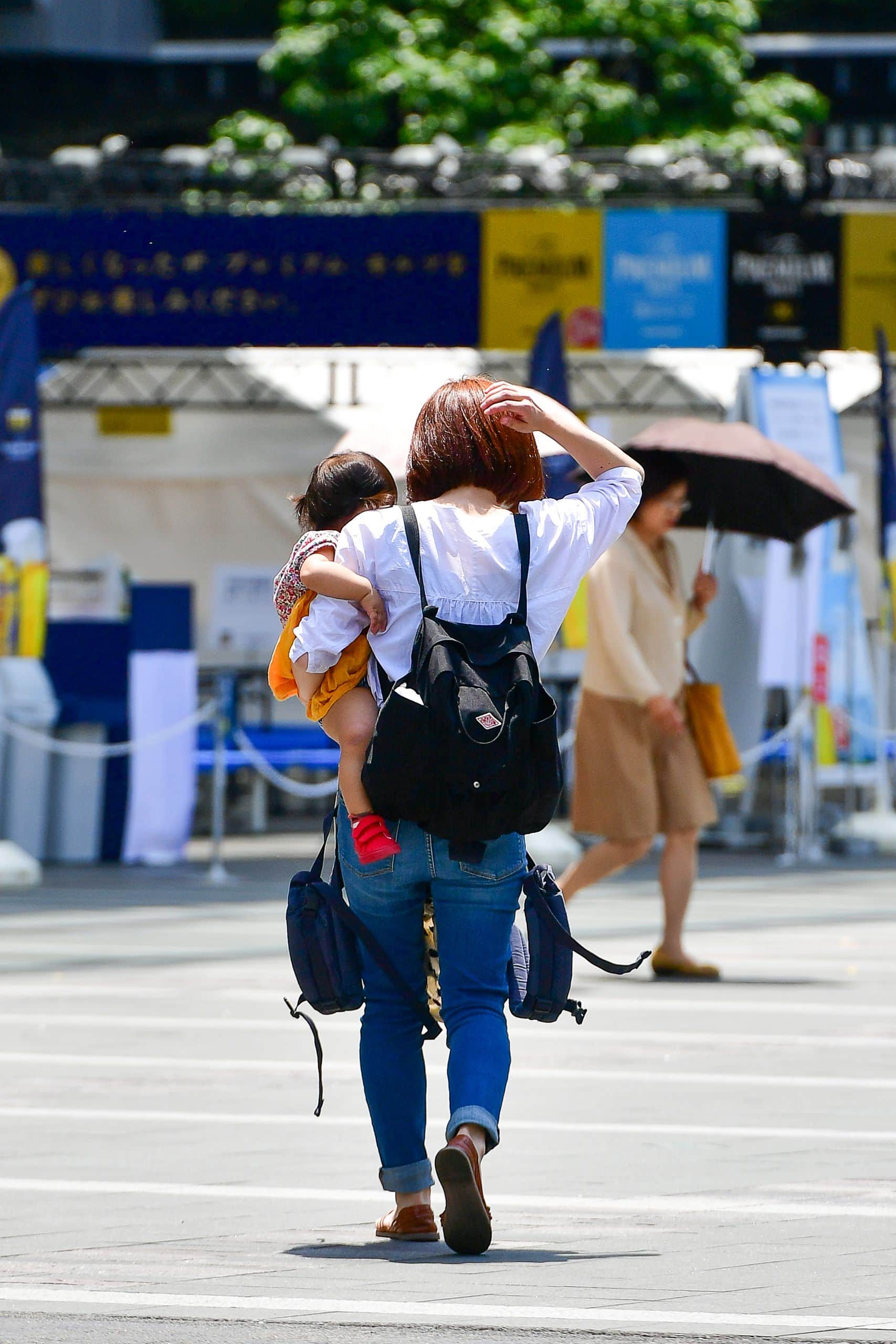 A candid scene of a mother carrying her child on a sunny day in Fukuoka's vibrant urban square.
