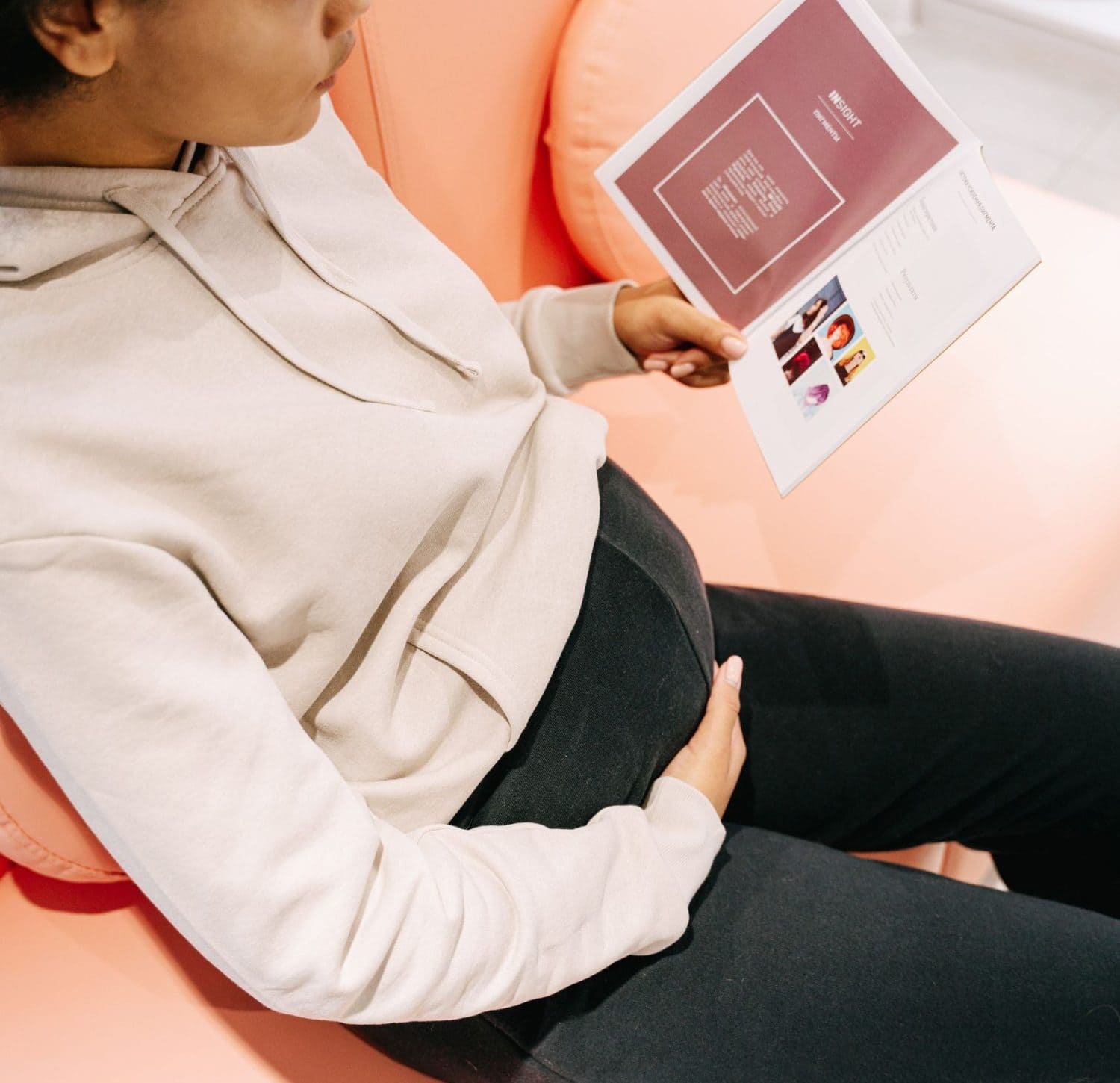 A pregnant woman sits comfortably indoors reading a brochure, symbolizing information gathering during pregnancy.