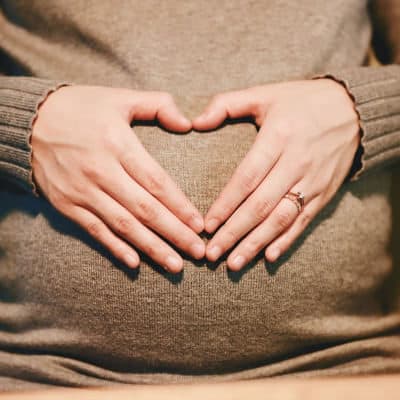 A pregnant woman with her hands over her womb, forming a heart shape