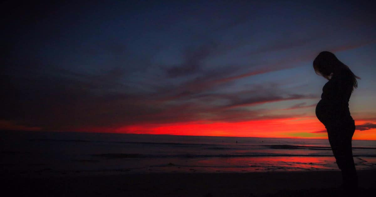 A picture of a pregnant woman at sunset.