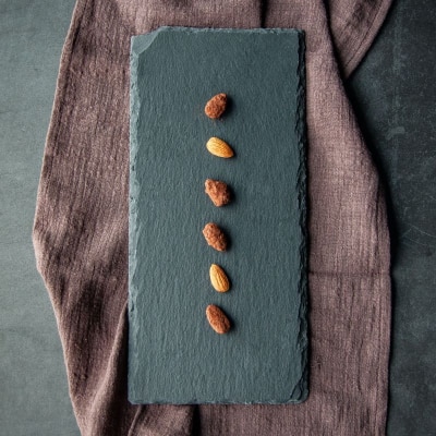 six almonds on a slate slab; there is a brownish napkin beneath