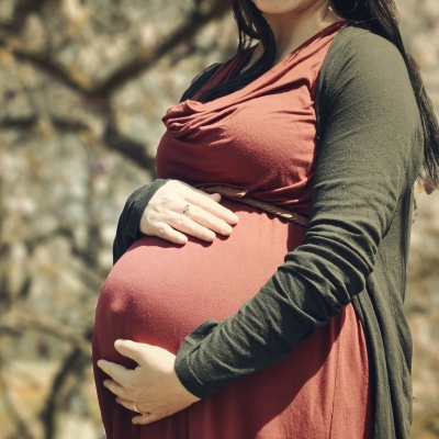 A photo of a  pregnant lady wearing a brown dress and green cardigan