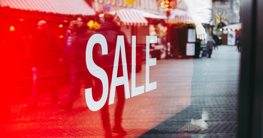 a store sign in window that reads SALE; window is reflecting the city street and photographer