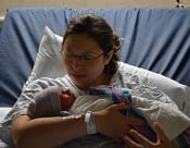 A woman holding her infant child while lying on a hospital bed