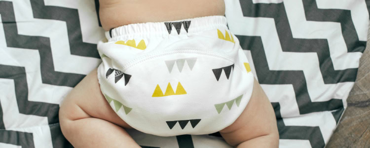 baby wears cloth diaper with gray yellow pattern on it while crawling across a chevron baby blanket