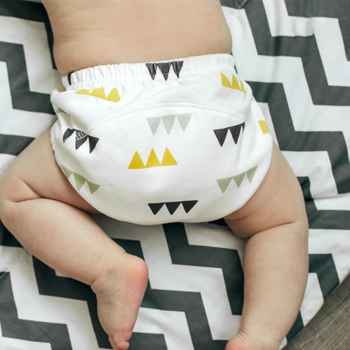baby wears cloth diaper with gray yellow pattern on it while crawling across a chevron baby blanket