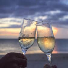 2 champagne glasses clinking; the ocean and sunset are in the distance