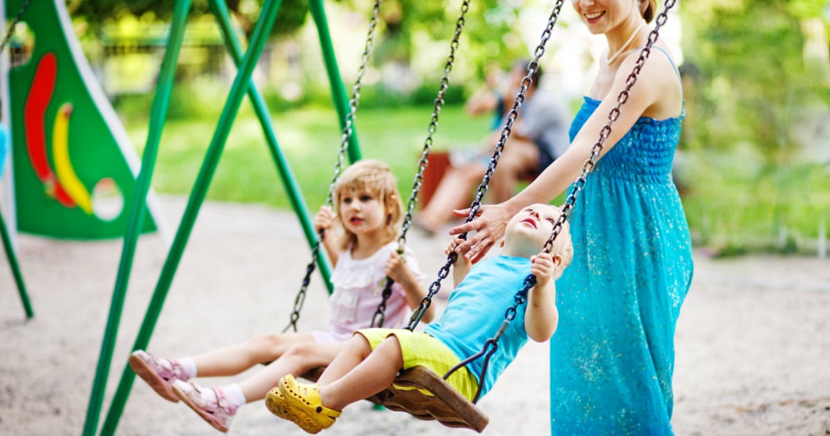 laid back mom pushing child on swings