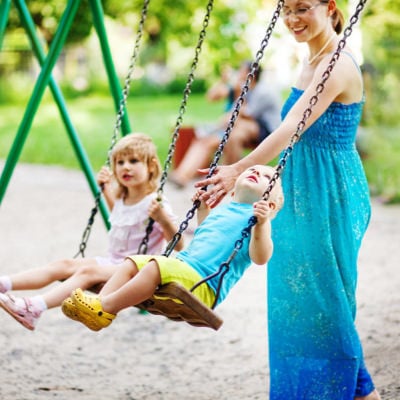 A woman with two kids playing on swings