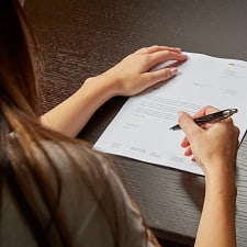 A woman writing on a white paper with a pen