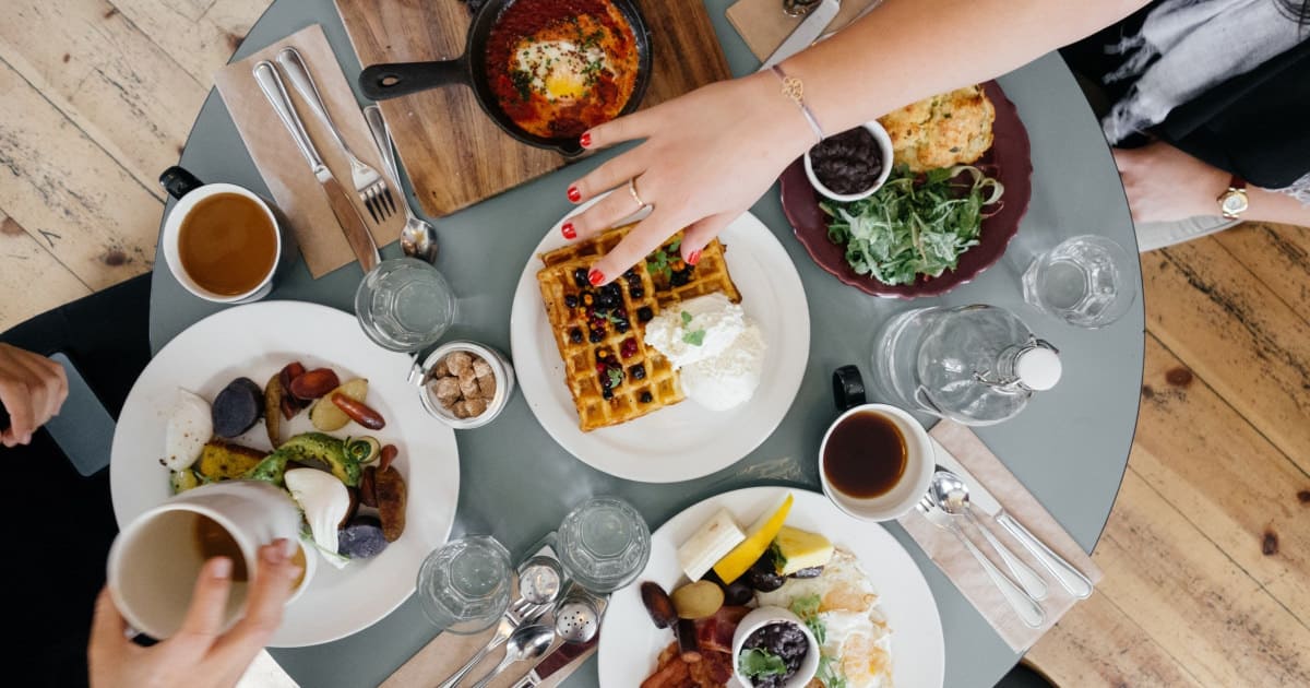 stock photo of aerial view of brunch table with hands reaching for waffles and coffee