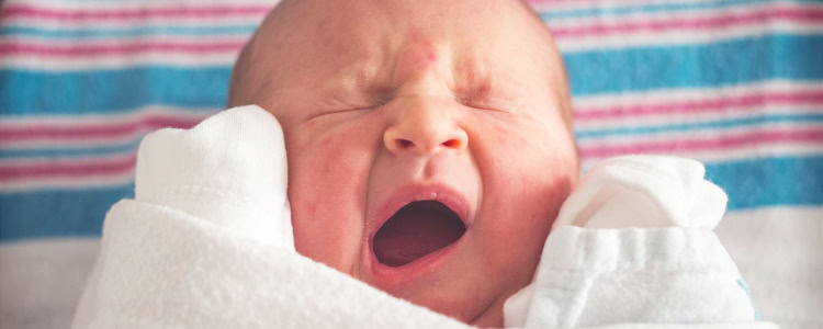newborn baby yawns (or cries?); they are laying on the typical white, pink and blue hospital swaddle
