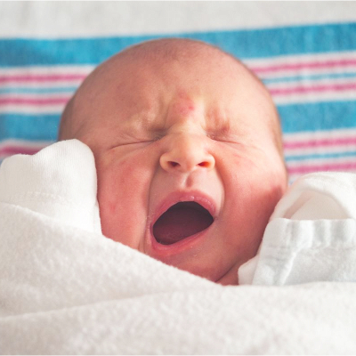 newborn baby yawns (or cries?); they are laying on the typical white, pink and blue hospital swaddle