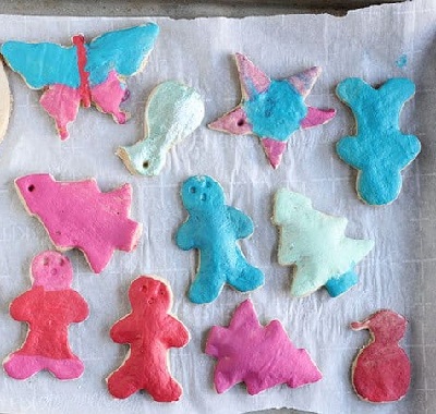 Salt dough Christmas ornaments painted in white, blue, pink, and red and placed on a baking tray with parchment paper