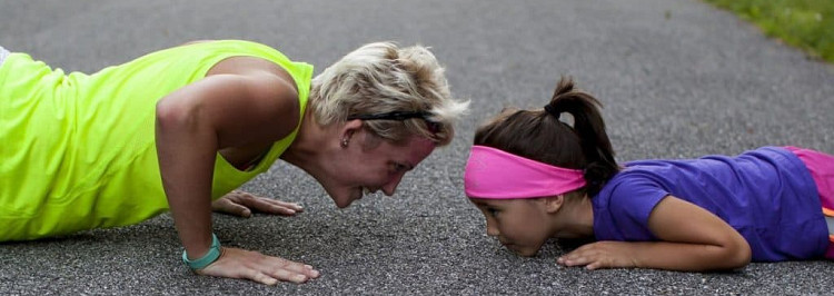 woman and child do push ups opposite each other; the adult wears a neon yellow top and the child wears a bright pink headband, purple shirt, and has a ponytail