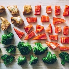 A table of food with chicken, broccoli, and red pepper.