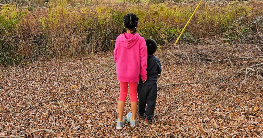 Two children, one in pink and one in black, look away from the camera in a field 
