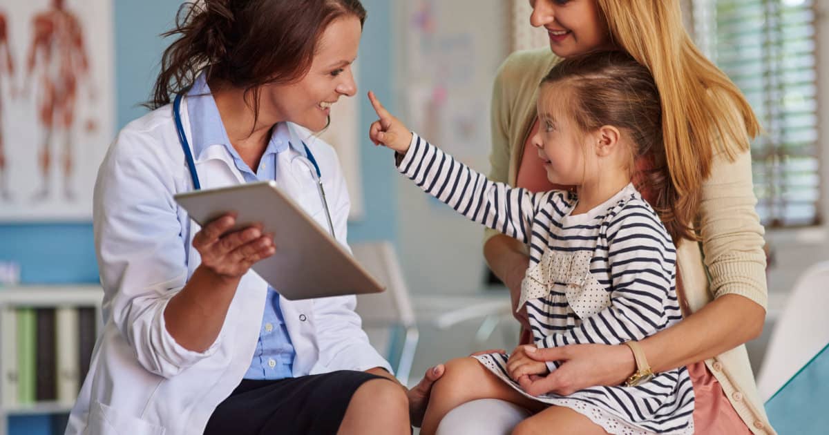 stock photo of a little girl touching a female doctor's nose while her young professional mother holds her