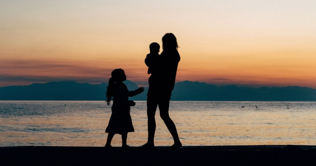 A beach scene with a woman and two kids silhouetted in the light 