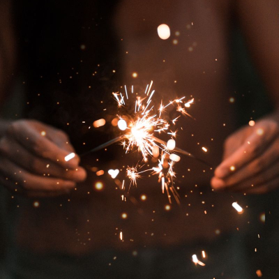 person holding sparkler candle; you can see their hands and a number of sparks flying everywhere