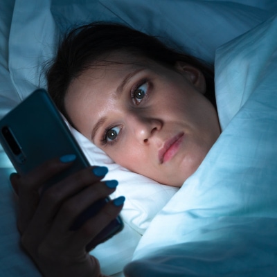 woman in bed checks phone