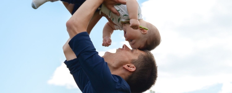 man swings baby up; their foreheads touch