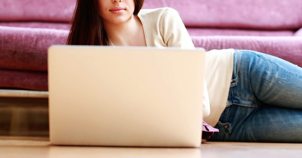 young professional mom lying on floor working on laptop in front of purple couch