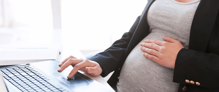 professional pregnant woman wearing a blazer, with one hand on a keyboard and one hand on her belly