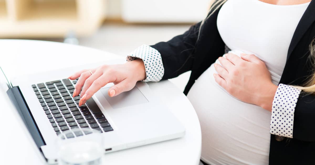 pregnant professional woman wearing a blazer and working on a laptop