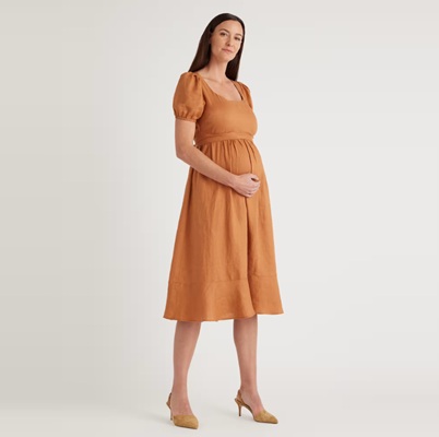A pregnant woman wearing a rust-brown dress and sandals