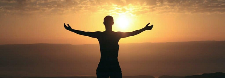 man salutes the sun with his arms spread wide. 