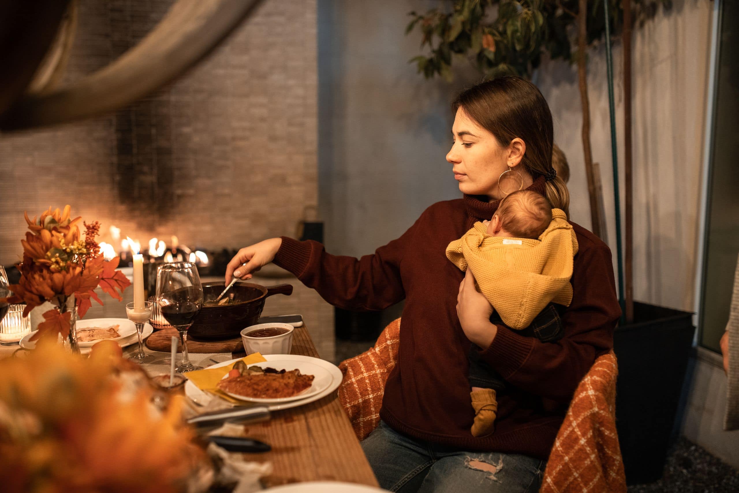 Mother holding baby during a warm indoor dinner by the fireplace.