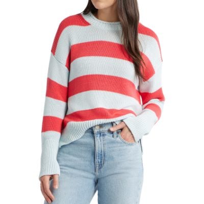 A woman wears a boldly striped sweater in red and blue with light blue jeans