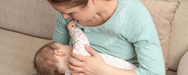 mom holds baby who is tugging at mom's light green shirt