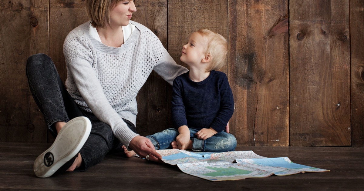 young professional mom making a silly face at her blond toddler son while they look at a map