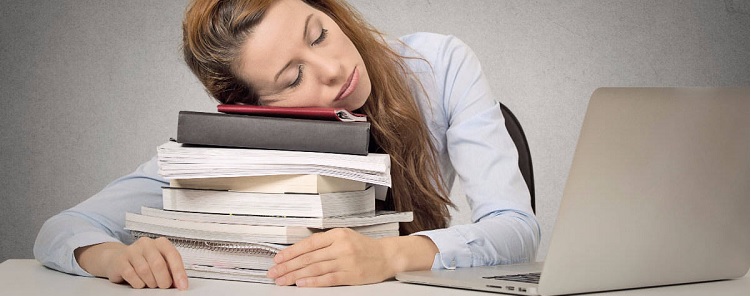 professional woman asleep on pile of books with laptop open in front of her.