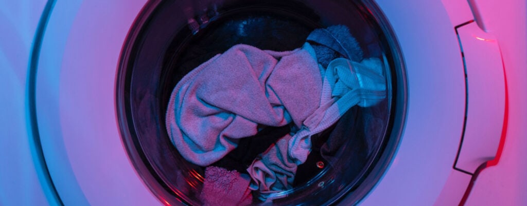 close-up focus on the window of a washing machine with clothes inside... there is a purplish light in the room