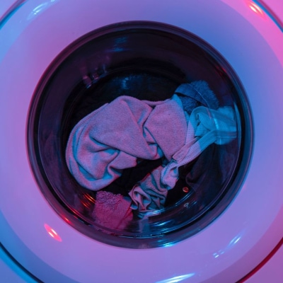 close-up focus on the window of a washing machine with clothes inside... there is a purplish light in the room