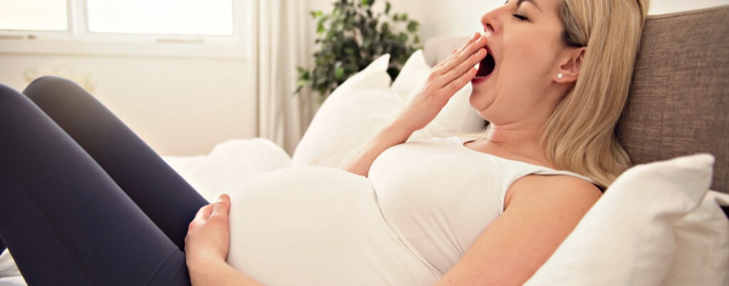 tired pregnant woman yawning, she is dealing with fatigue in pregnancy