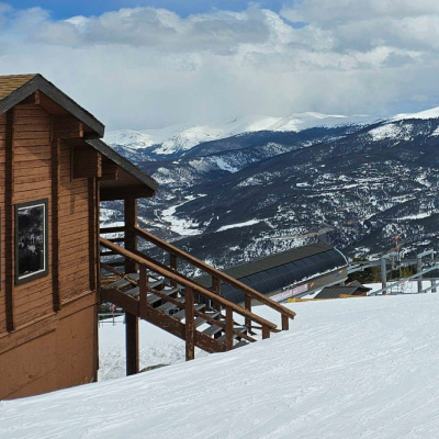 A view of snow-capped mountains from a snowy area next to a cabin at a ski resort