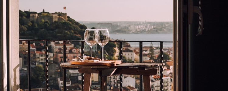 two wine glasses on a table on a balcony overlooking a mountain vista (maybe Italy)