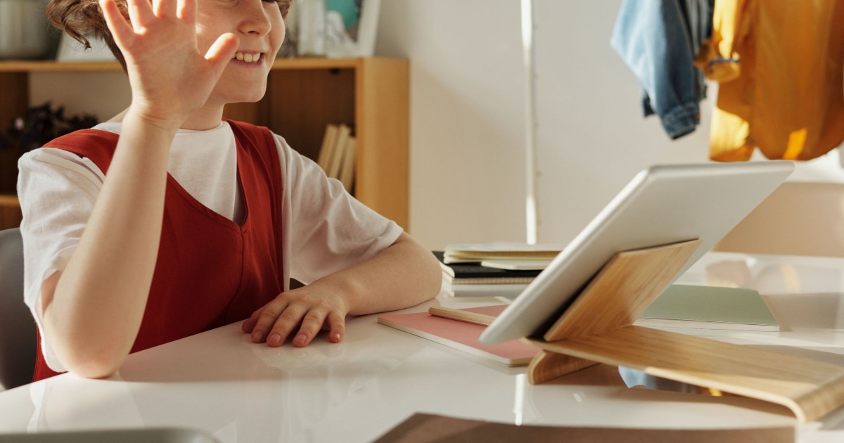 child in front of ipad, smiling and waving hello