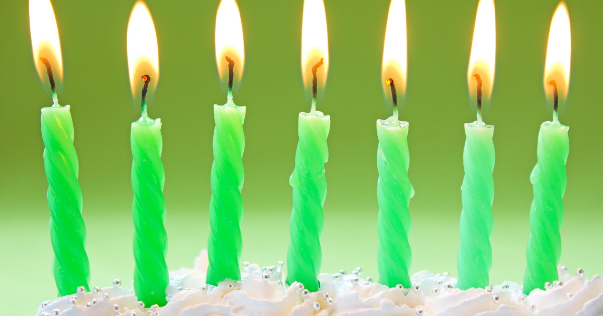 seven green, lit candles on top of a fluffy white cake 