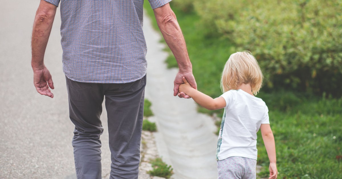 man walks down a path; he is holding the hand of a blonde toddler