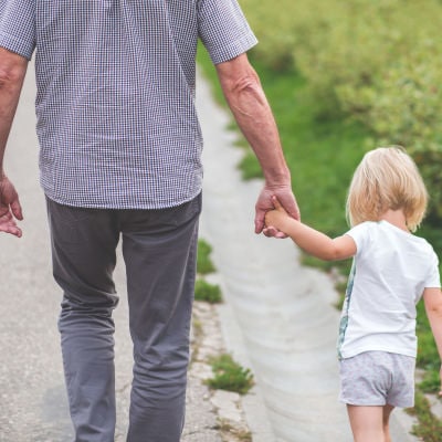 man walks down a path; he is holding the hand of a blonde toddler