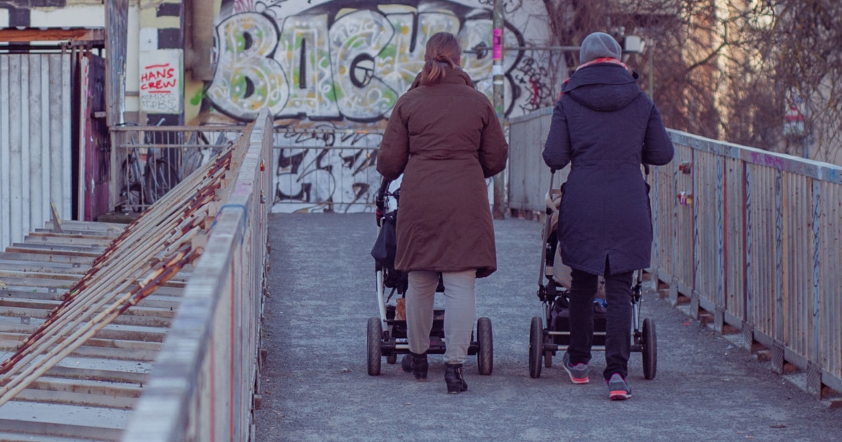 two women walking with strollers in an urban environment