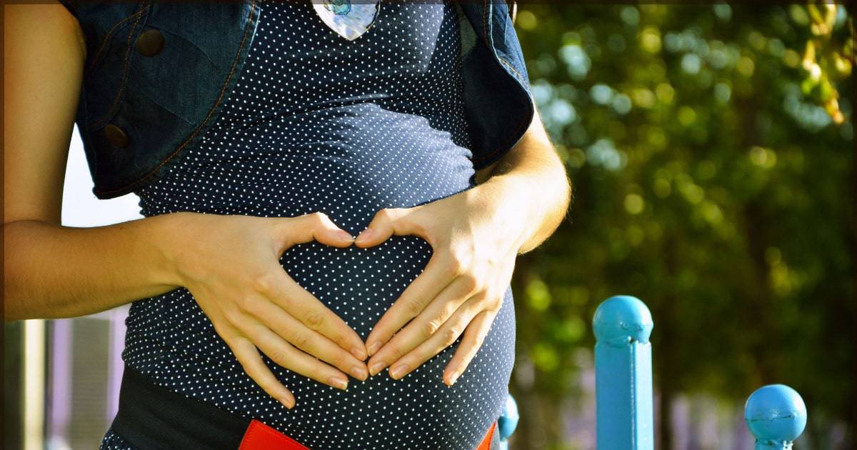 A pregnant woman posing with a heart sign on her hands.