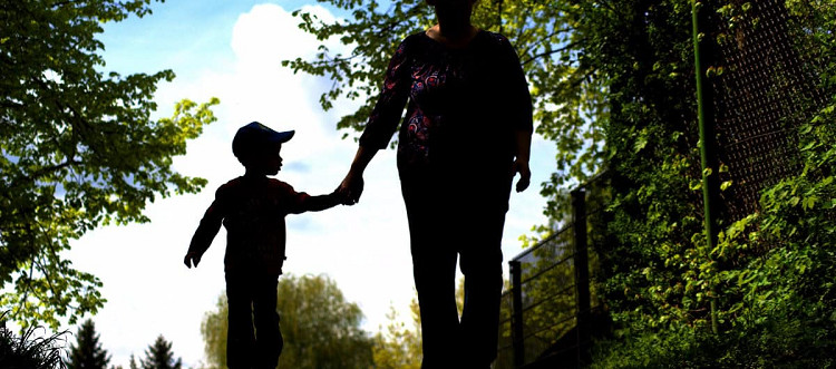woman holding hands with little boy; they are walking outside and in shadow